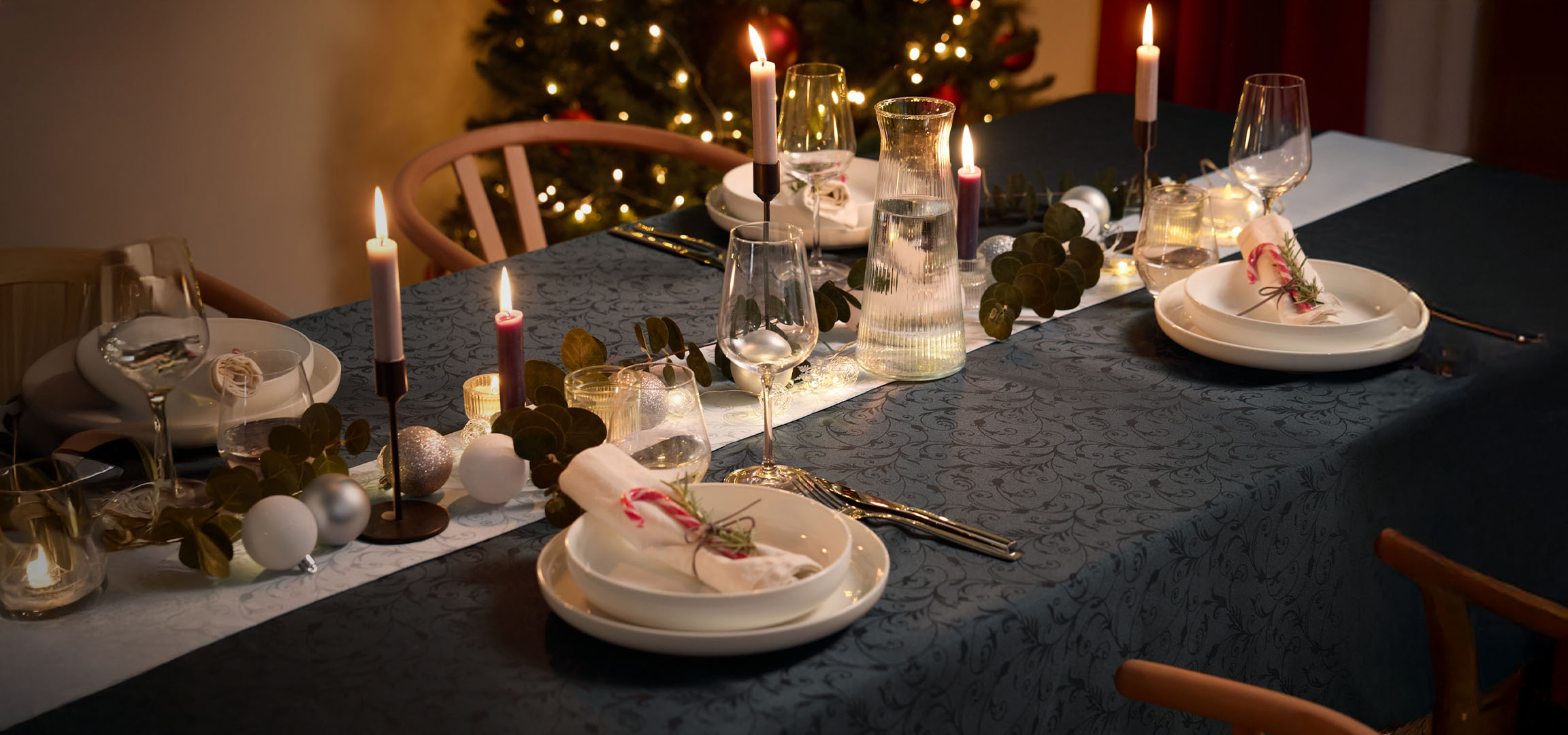 Table de Noël avec bougies, vaisselle blanche et décorations festives.