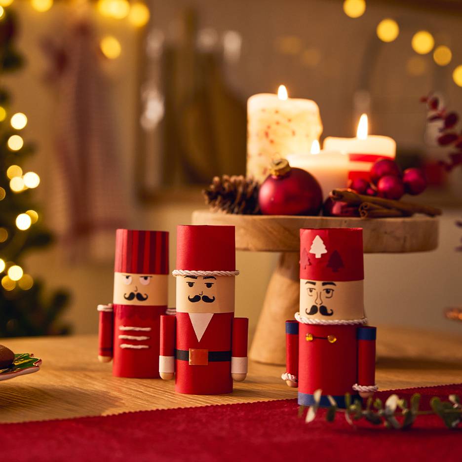 Trois casse-noisettes en papier sur une table avec des décorations de Noël et des bougies allumées.