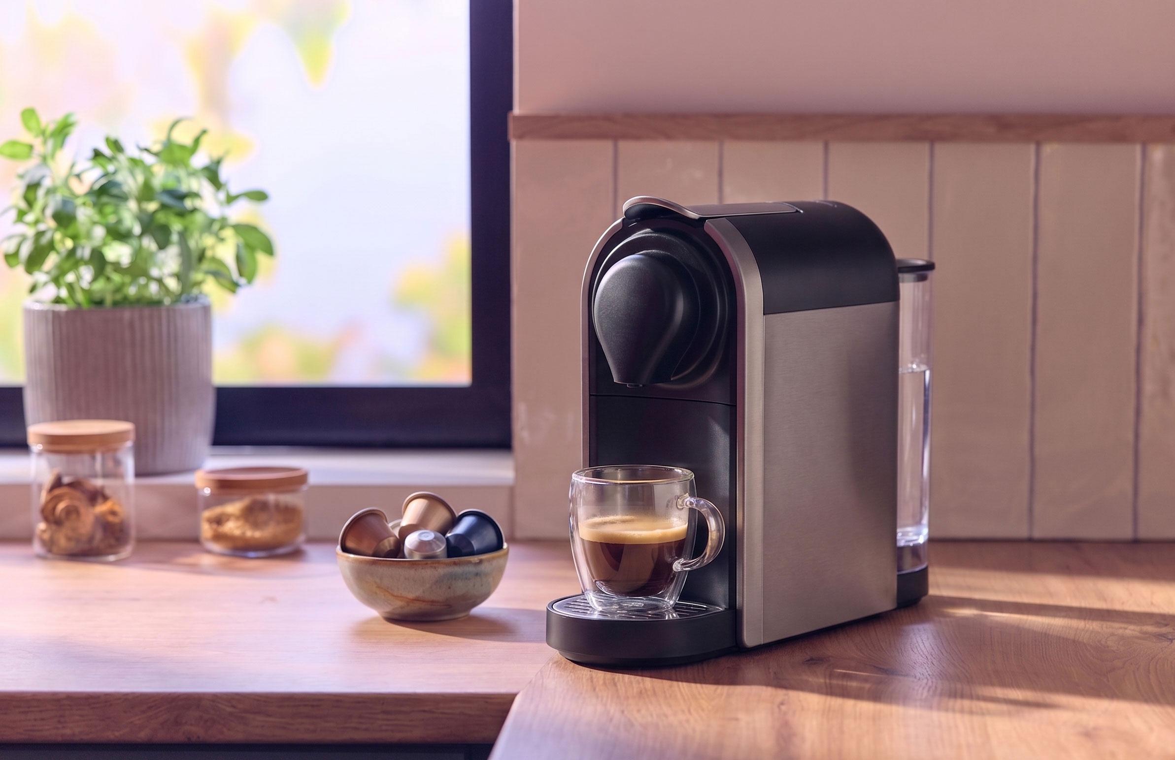 Machine à café avec une tasse de café, des capsules et des bocaux sur un comptoir en bois.