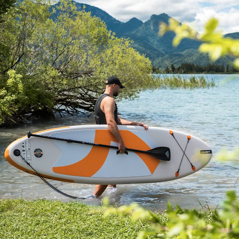 Homme avec planche de paddle CRIVIT dans l'eau, prêt à pagayer.