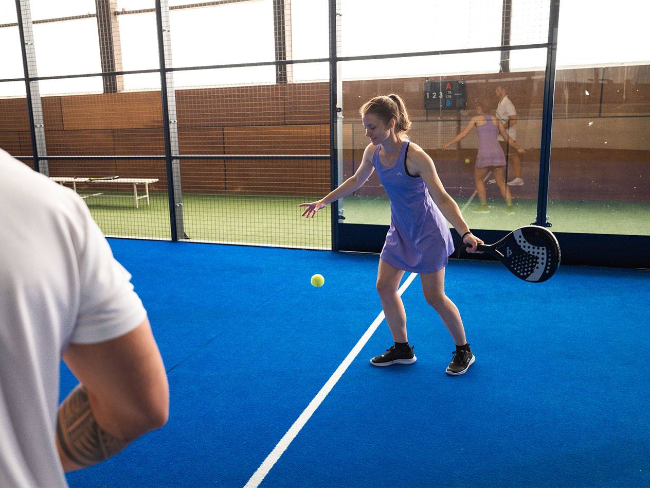 Femme en robe de sport violette jouant au padel avec raquette et balle.