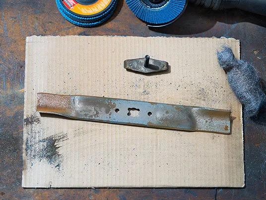 Lame de tondeuse rouillée sur carton avec disques abrasifs et laine d'acier.