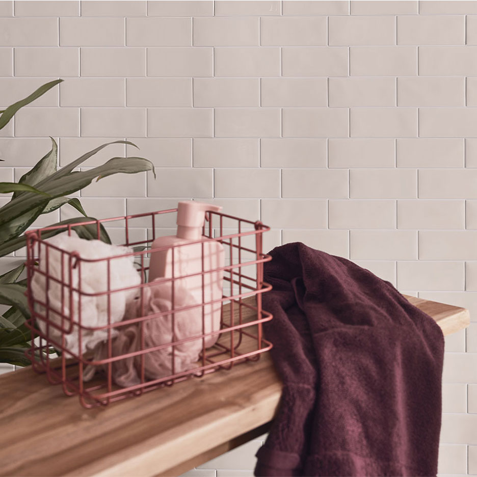Décor de salle de bain avec carrelage blanc, banc en bois, panier avec savon et serviettes.