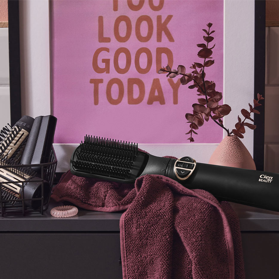 Brosse lissante Cien Beauty sur une serviette, avec accessoires pour cheveux et un poster.