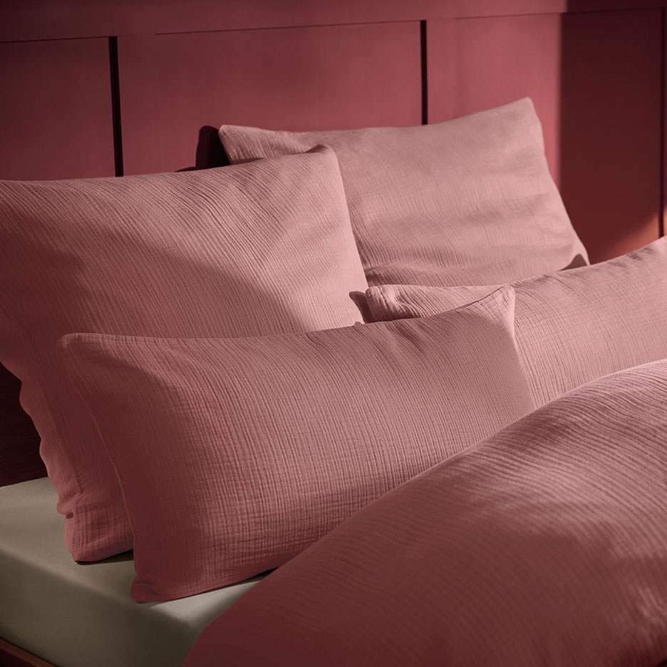 Oreiller et linge de lit en mousseline rose sur un lit avec tête de lit en bois.