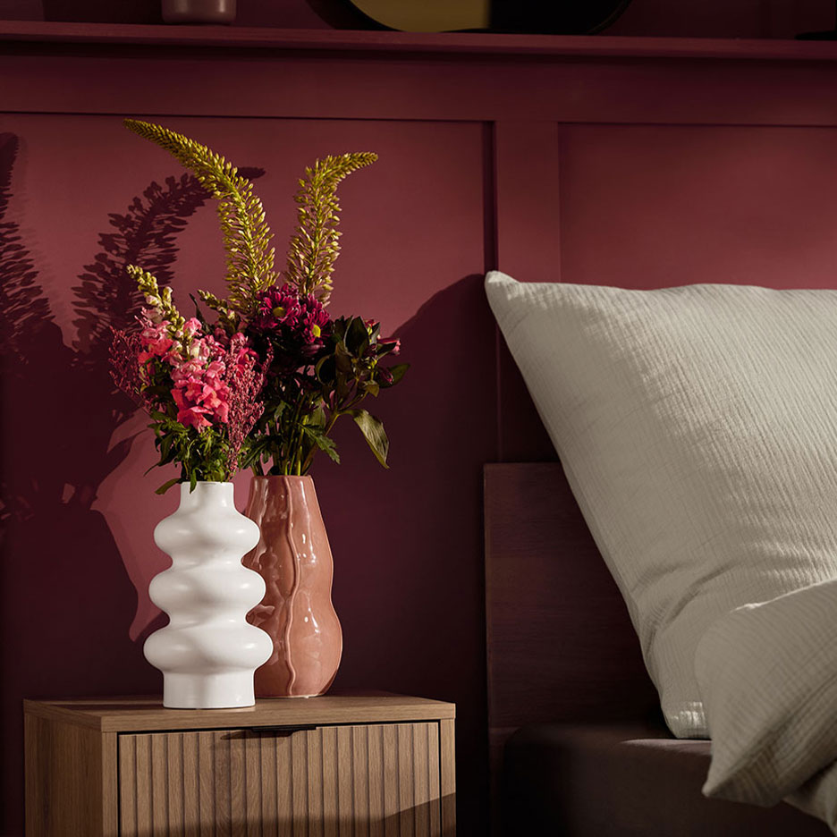Deux vases avec des fleurs sur une table de chevet à côté d'un lit avec un oreiller blanc.