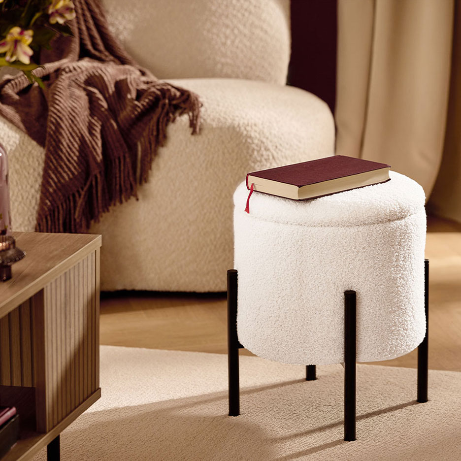 Tabouret blanc moelleux à pieds noirs, un livre rouge, fauteuil et couverture marron.