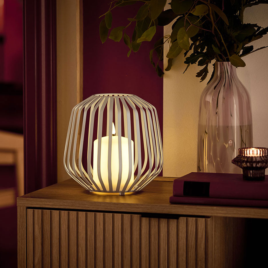 Une bougie LED dans un support métallique blanc sur une commode en bois.