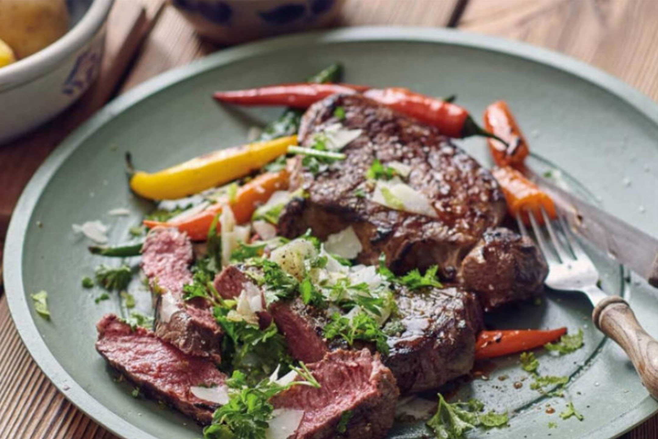 Steak grillé avec poivrons, herbes fraîches et copeaux de fromage sur une assiette verte.