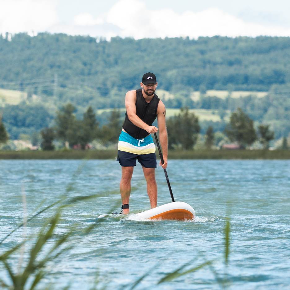 Homme faisant du stand-up paddle sur un lac, avec gilet de sauvetage et short de bain.