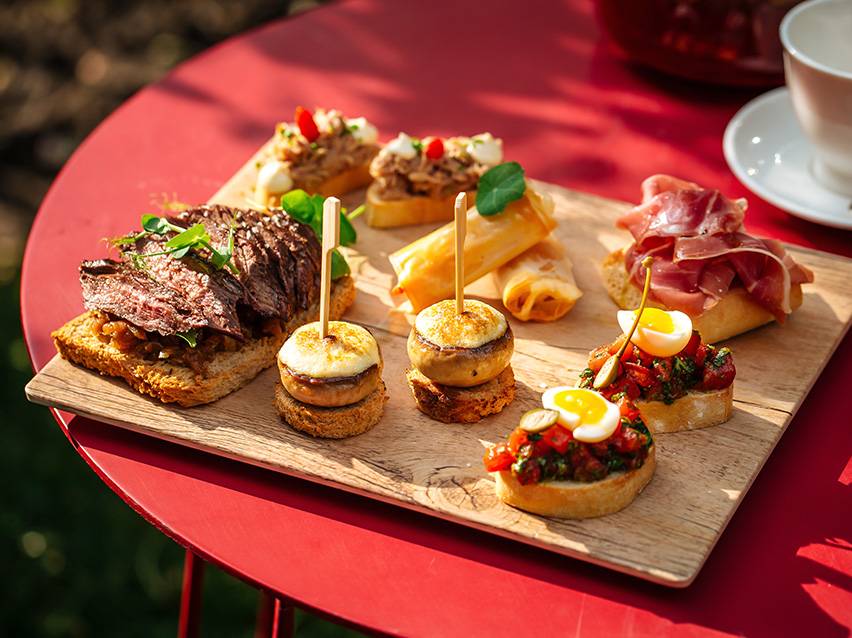 Assortiment de tapas et canapés, incluant steak, champignons, rouleaux de printemps et bruschetta.