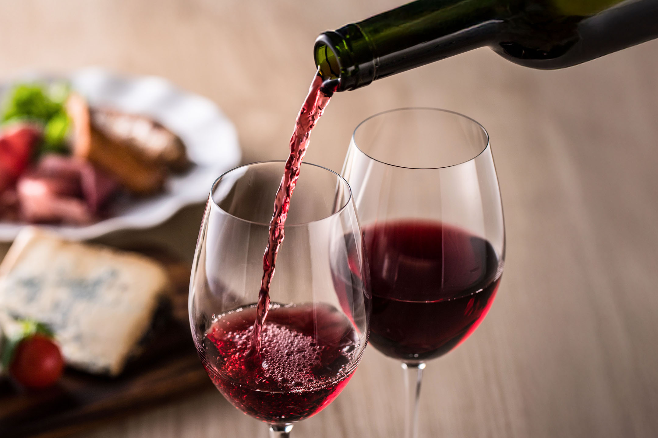 Vin rouge versé dans un verre, avec des amuse-gueules en arrière-plan.