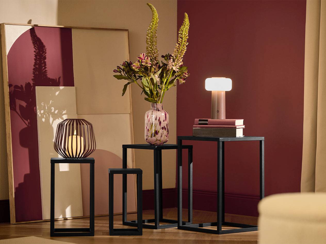 Trois tables d'appoint noires avec une bougie, un vase de fleurs et une lampe.