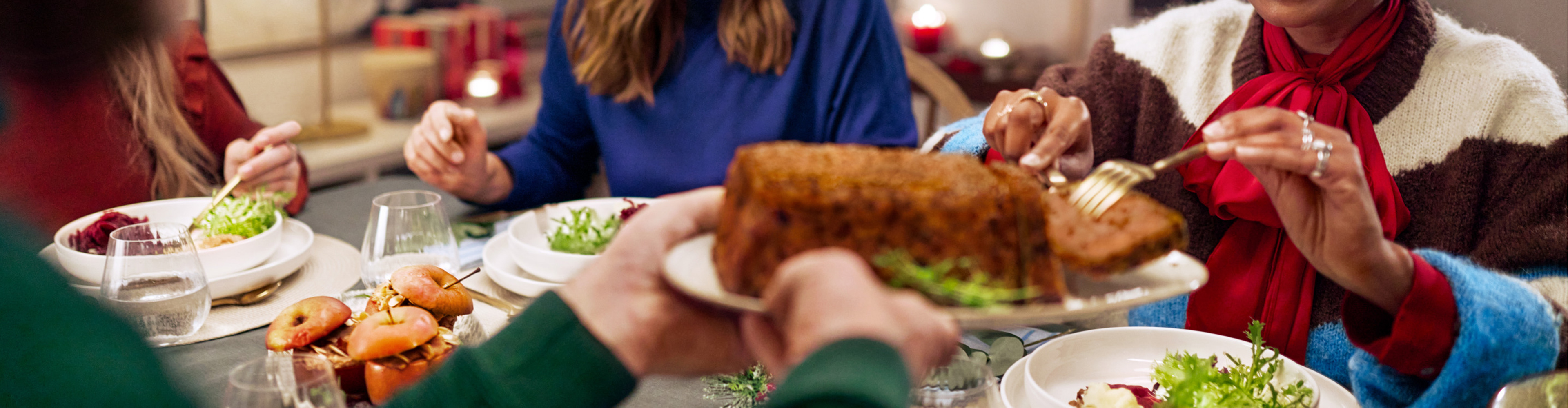 Deux femmes souriantes à table, l'une servant un plat principal, l'autre avec une salade.