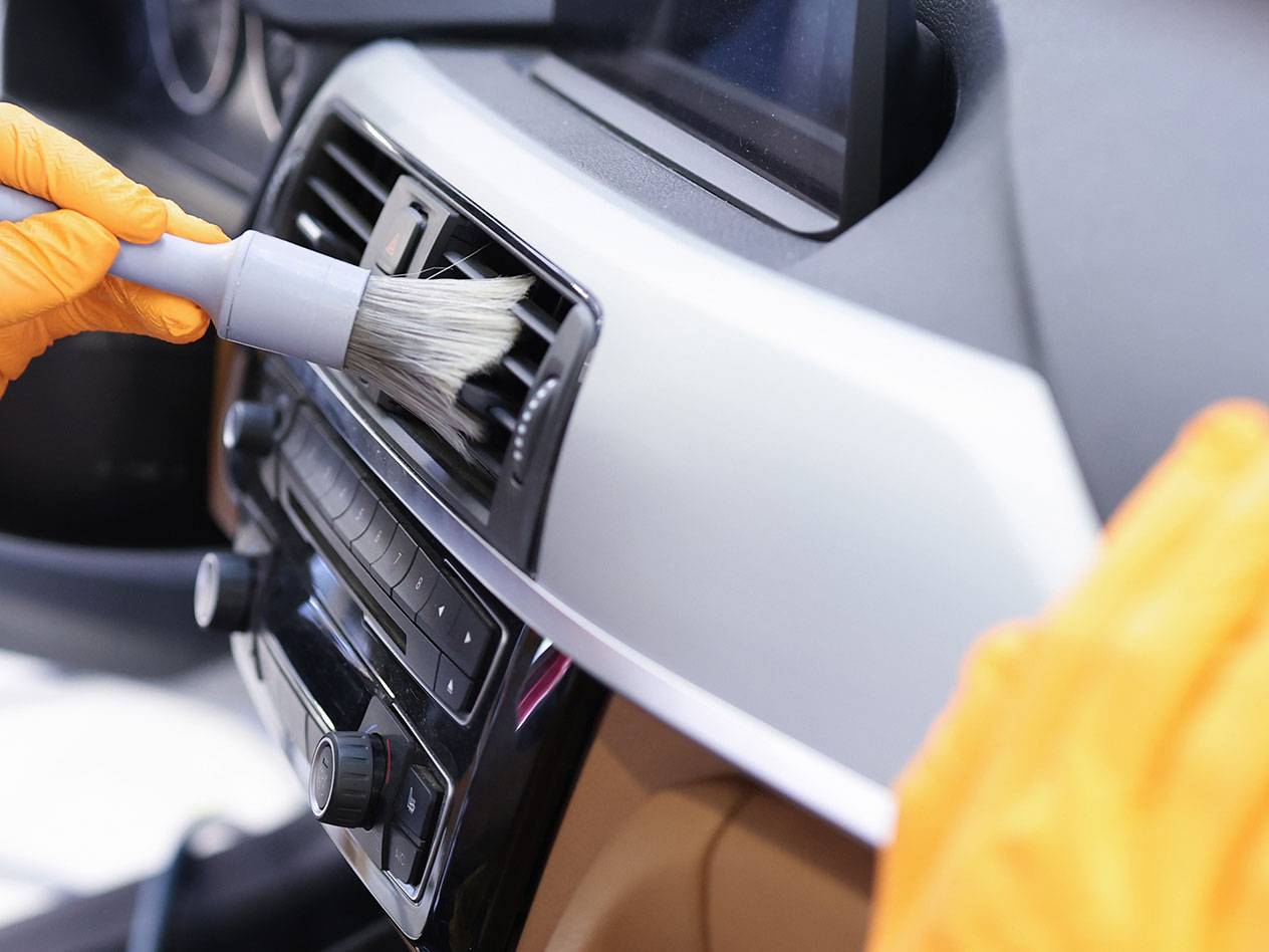 Nettoyage de l'intérieur d'une voiture avec une brosse de détail et des gants en caoutchouc.