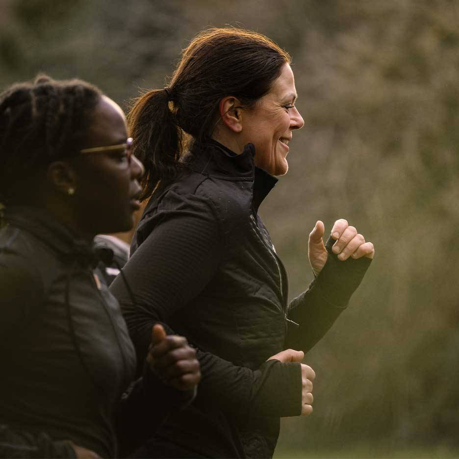 Deux femmes en tenue de sport courant en extérieur, l'une souriante.