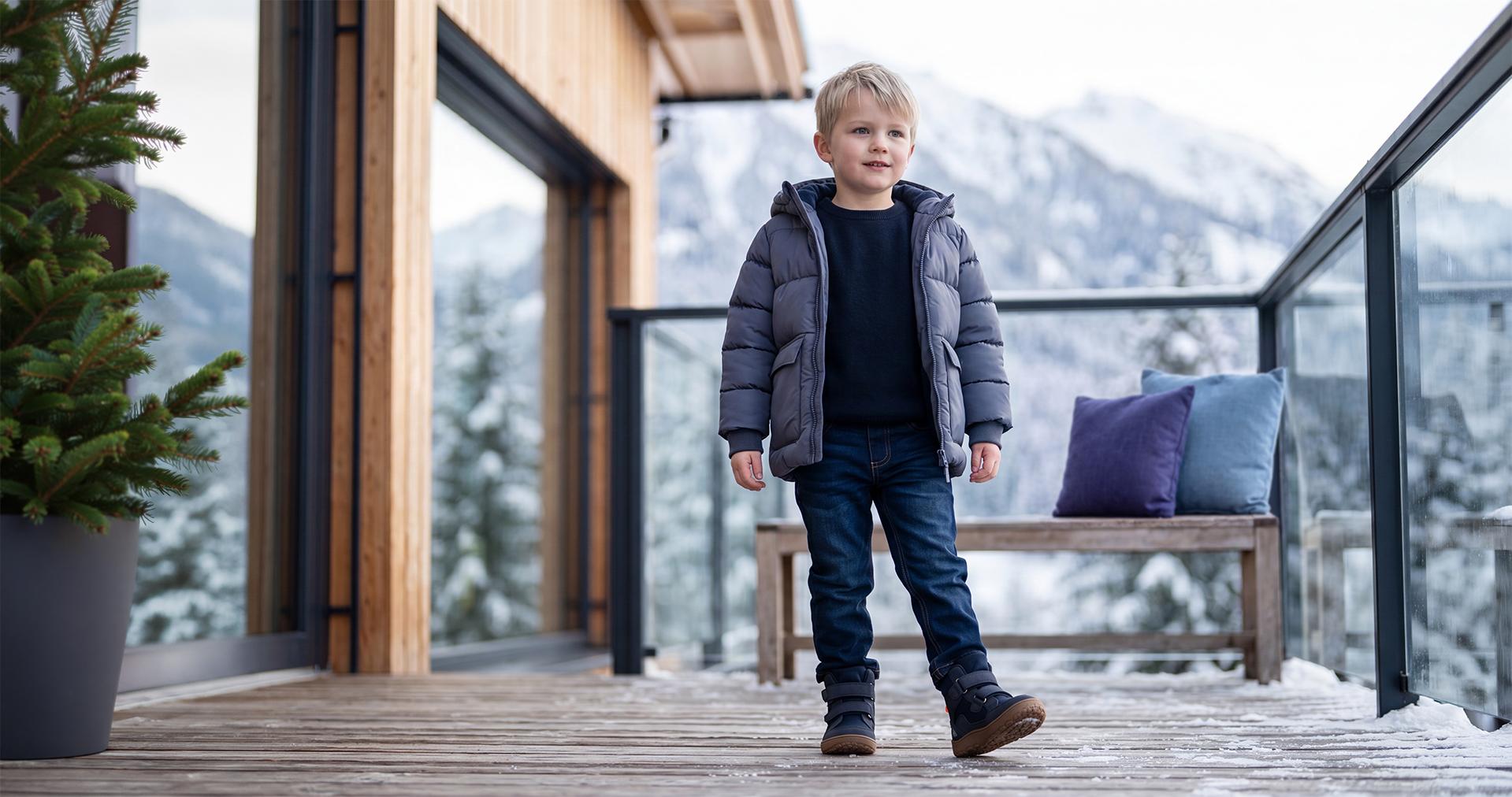 Petit garçon en veste d'hiver chaude, jean et bottes sur une terrasse de montagne