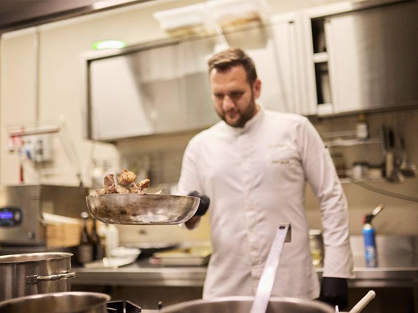 Un chef cuisinier en toque blanche fait sauter des aliments dans une poêle.