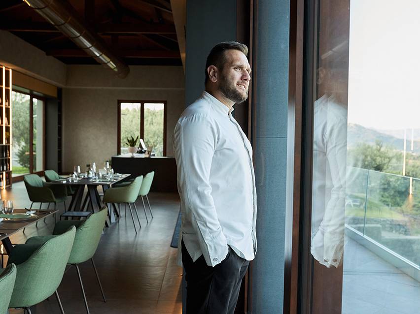 Homme en chemise blanche regardant par la fenêtre dans un restaurant avec des chaises vertes.