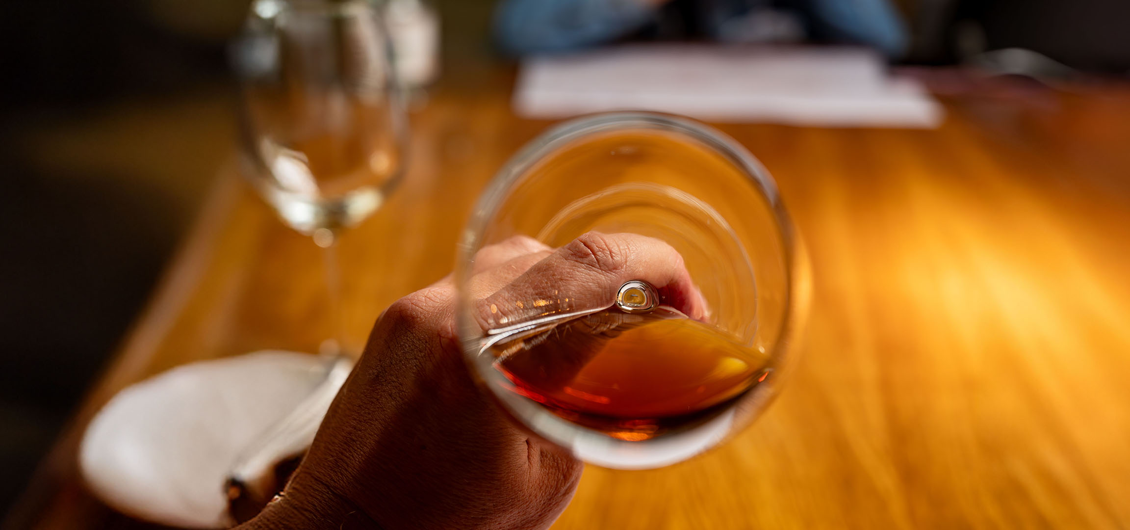 Gros plan d'une main tenant un verre de liquide ambré, peut-être du whisky ou du cognac.