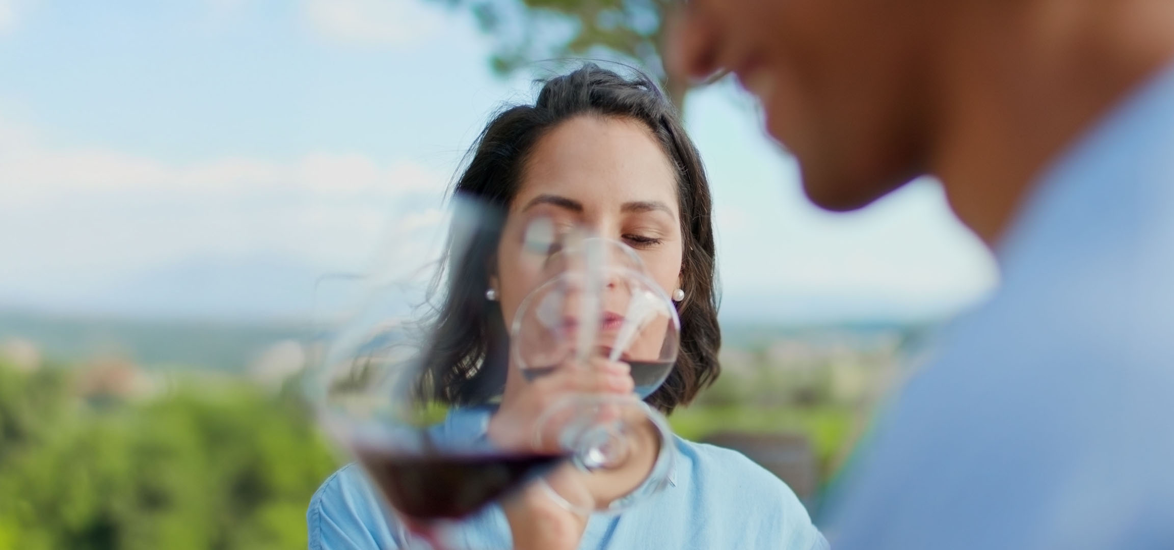 Femme dégustant du vin rouge en plein air, homme en arrière-plan.