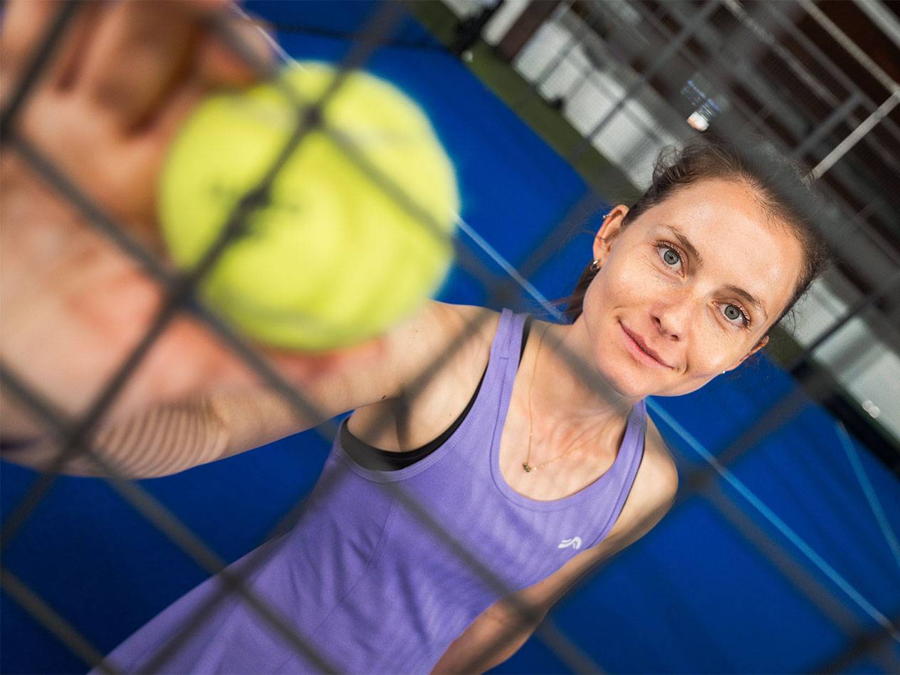 Femme sur terrain de padel tenant une balle de tennis jaune à travers le filet.
