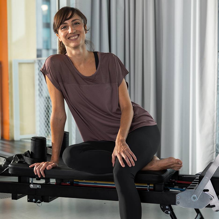 Femme en tenue de sport souriante assise sur un appareil de Pilates.