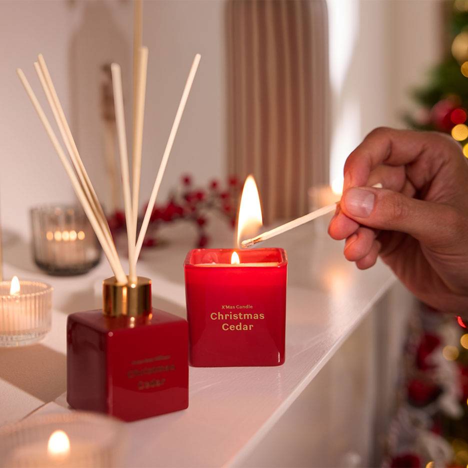 Diffuseur de parfum rouge et bougie 'Christmas Cedar' allumée avec une allumette.
