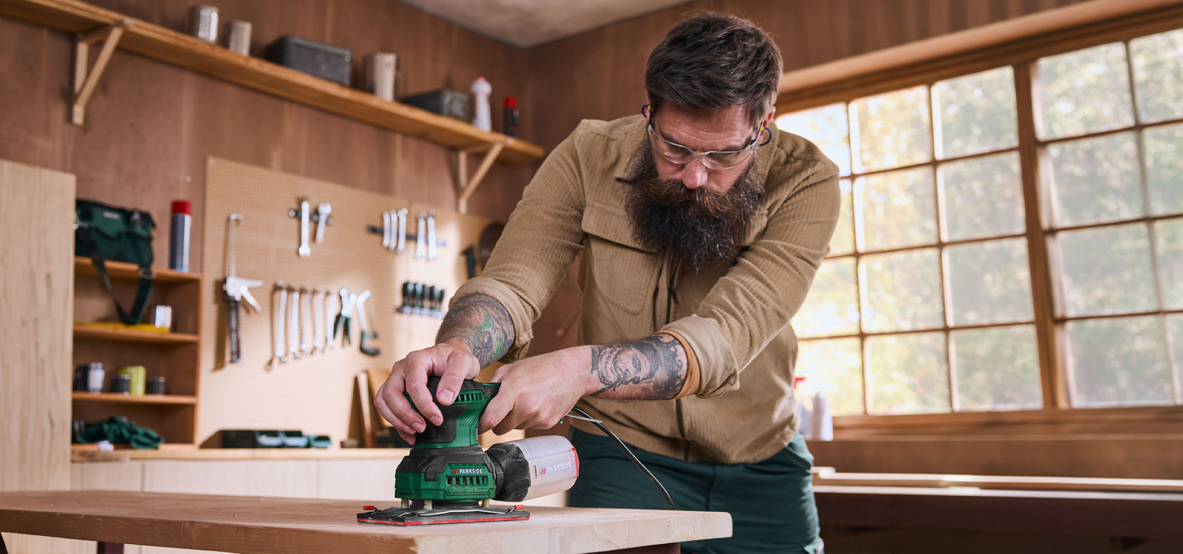 Un homme ponce une planche en bois avec une ponceuse électrique dans un atelier.