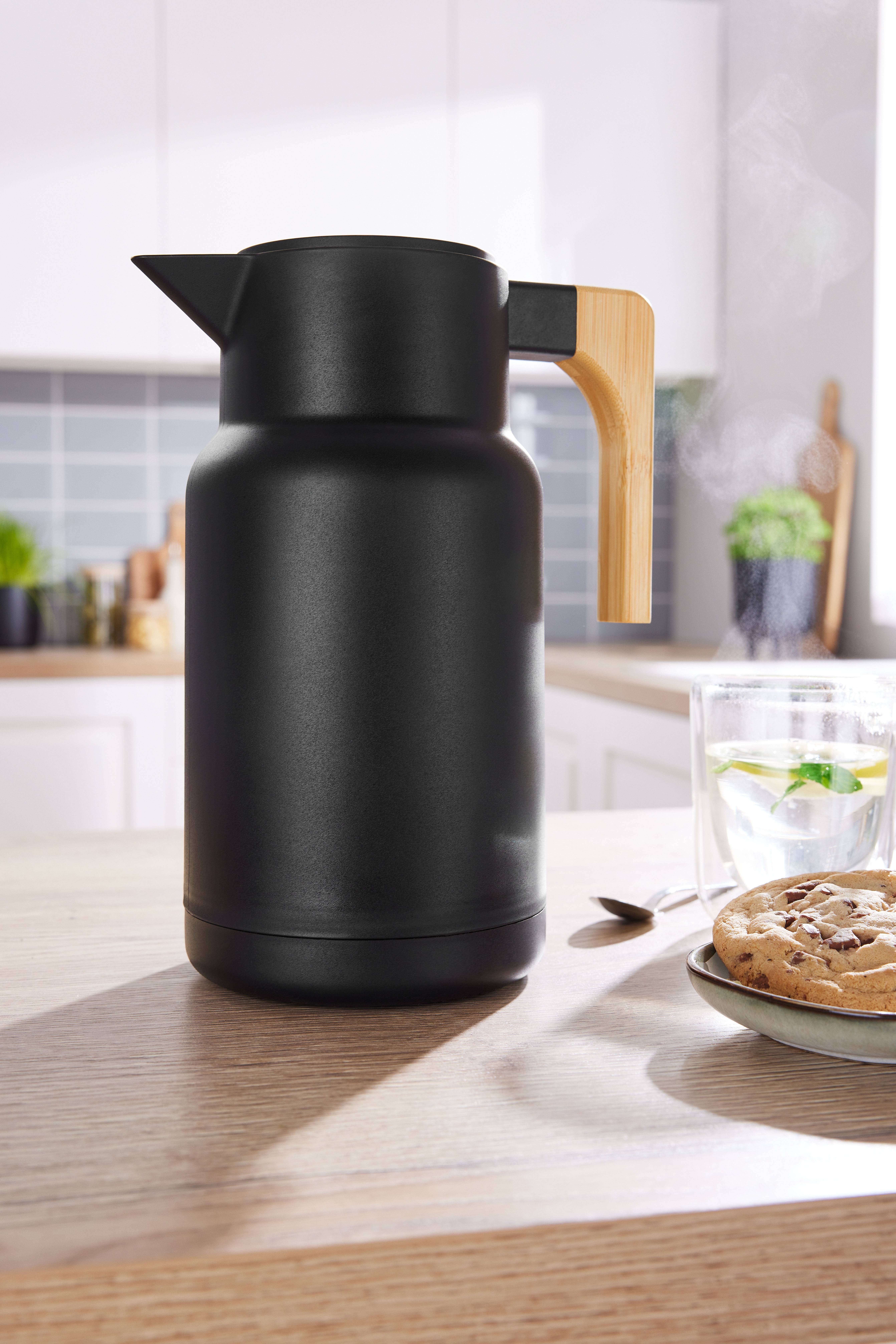 Thermos noir avec poignée en bois sur une table de cuisine avec des biscuits et du thé.