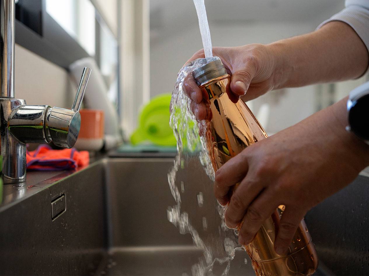 Personne remplissant une bouteille d'eau en cuivre au robinet dans un évier de cuisine.