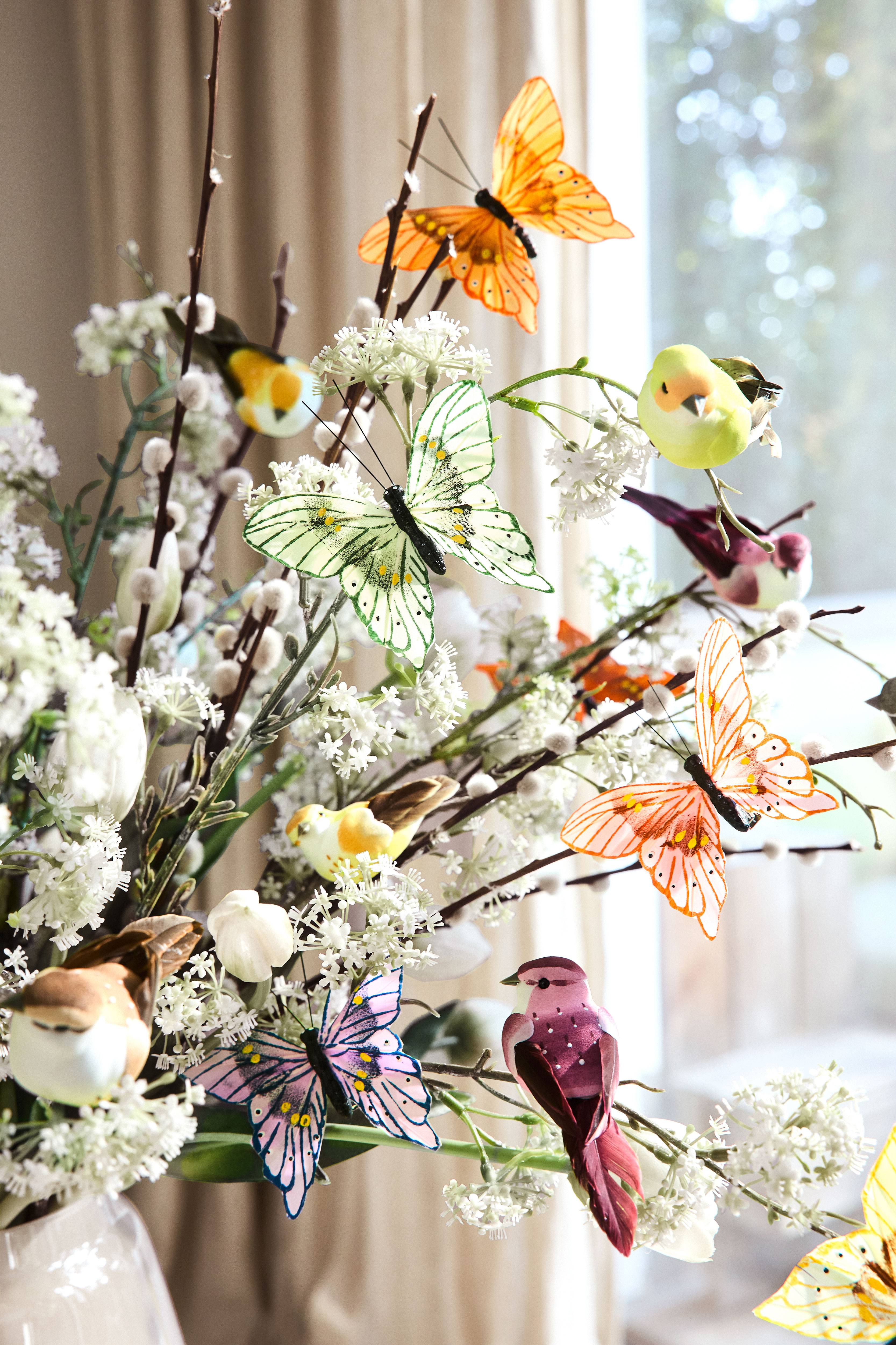 Décoration printanière avec papillons, oiseaux et fleurs artificiels dans un vase blanc.