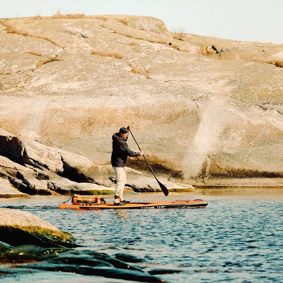 Homme pagayant sur une planche de paddle orange sur un lac rocheux.