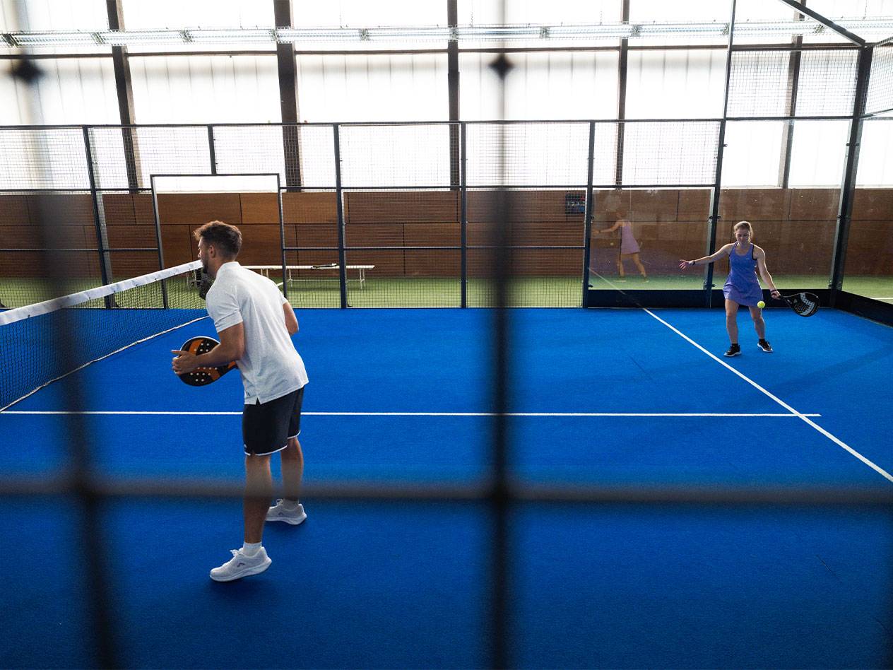 Homme et femme jouant au padel sur un court bleu avec raquettes et balle.