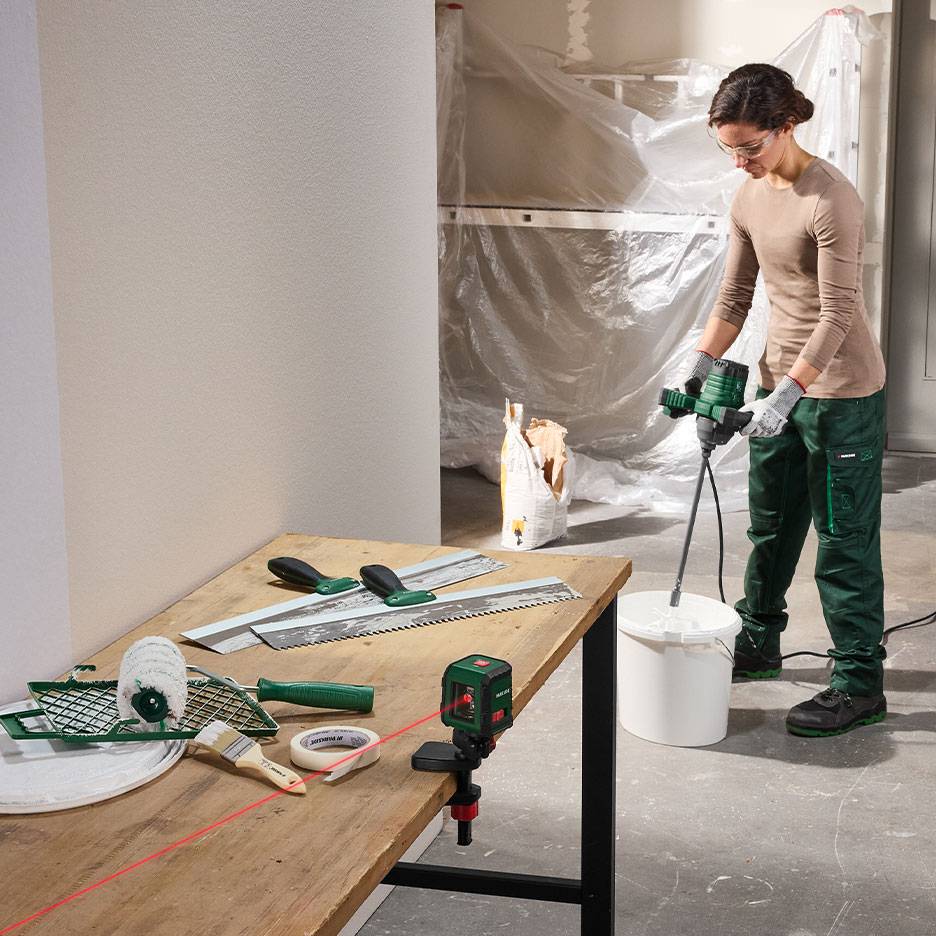 Femme mélangeant des matériaux de construction avec des outils de peinture et de nivellement sur une table.