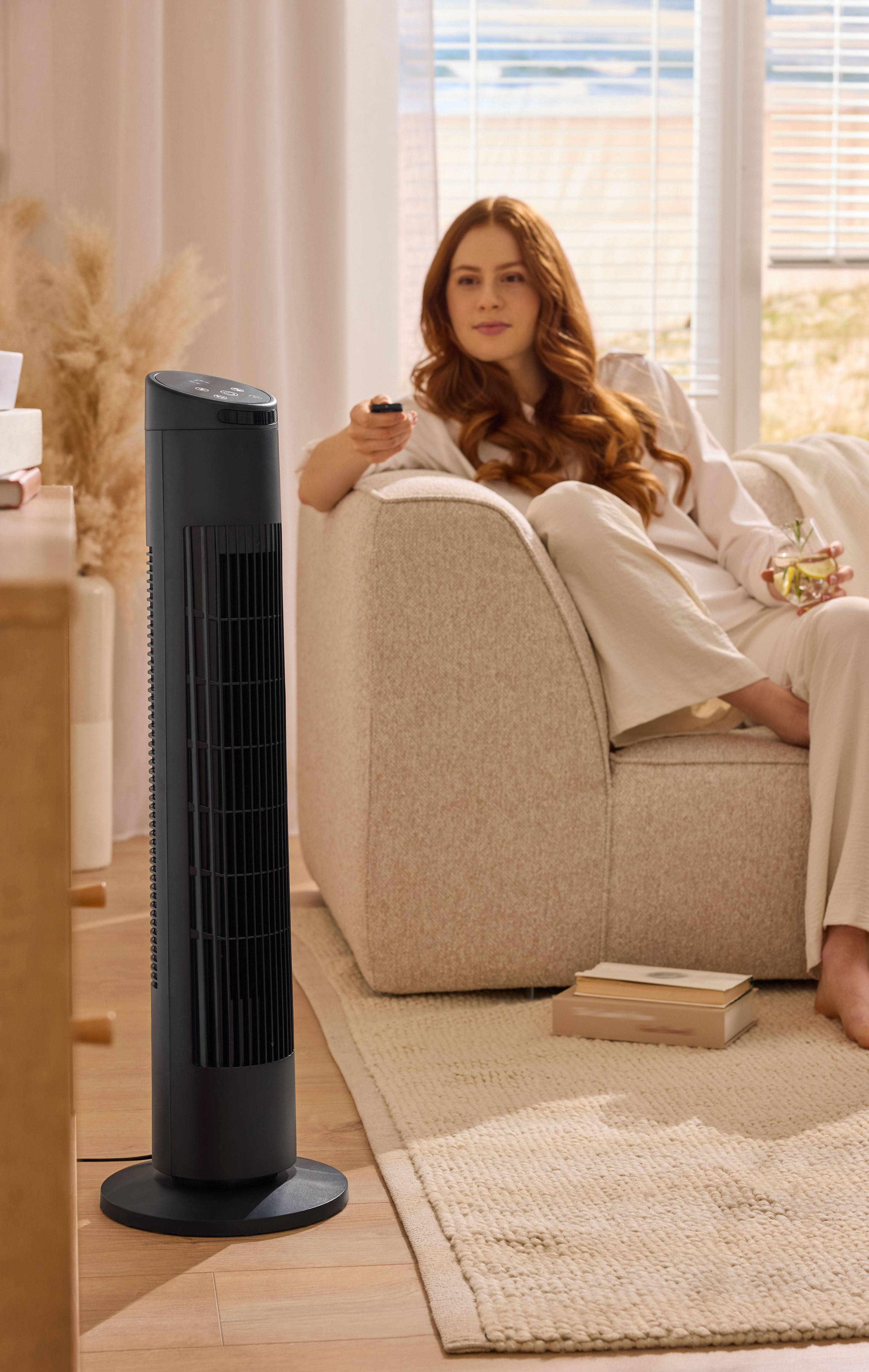 Femme se relaxant sur un canapé avec un ventilateur tour dans un salon.
