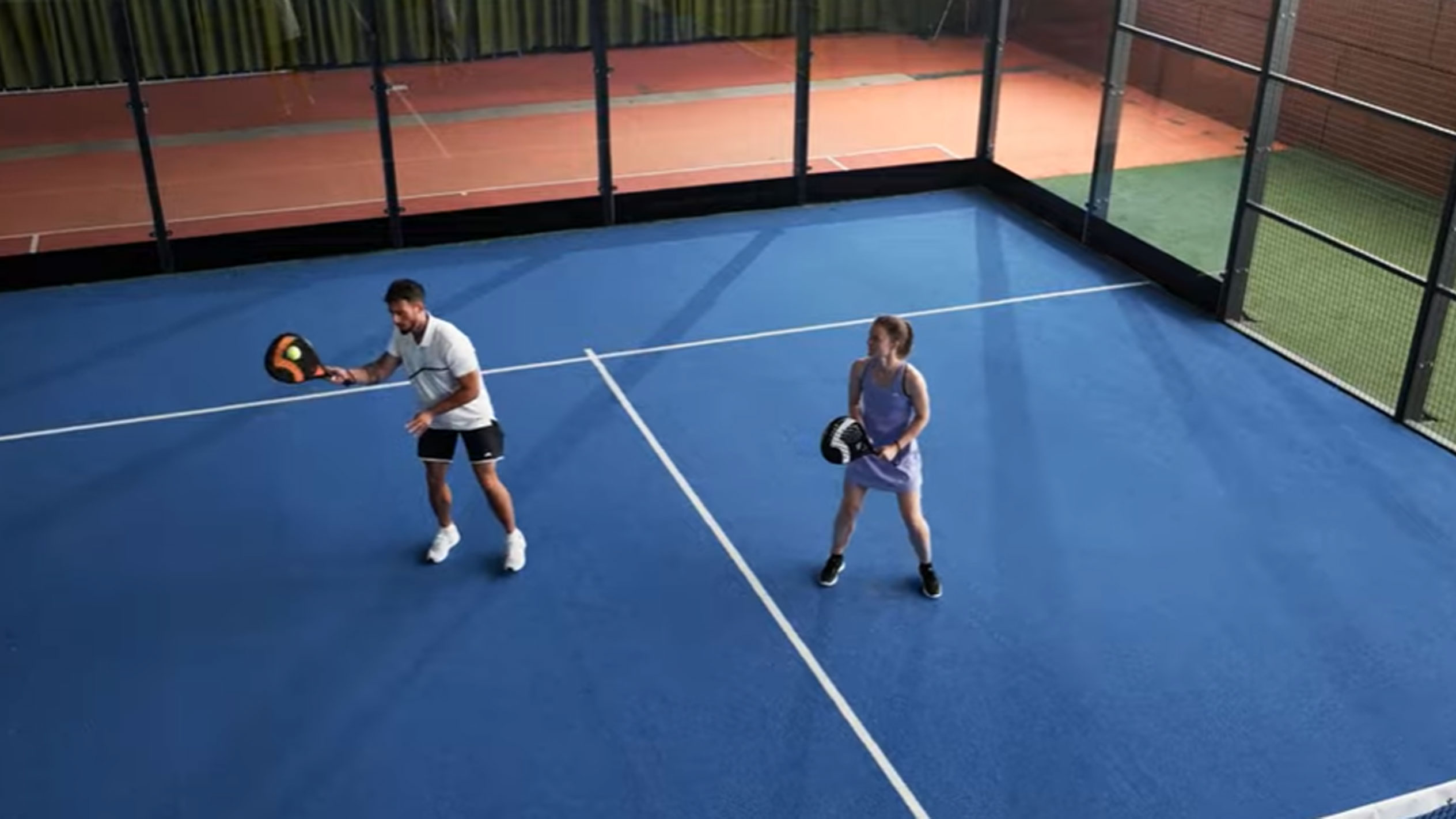 Homme et femme jouant au padel sur un court bleu avec raquettes et balle