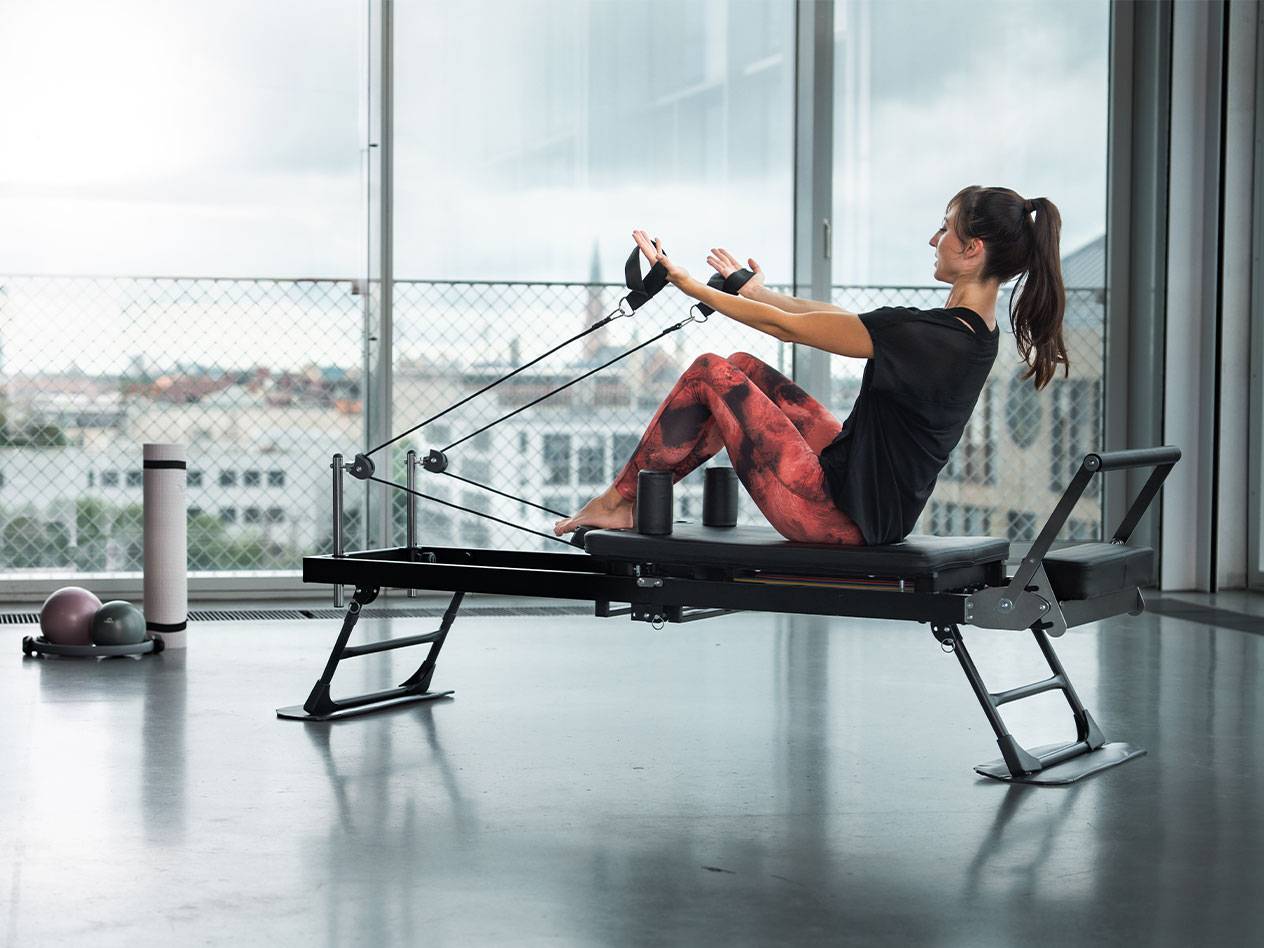 Femme faisant du Pilates sur un reformer avec vue sur la ville.