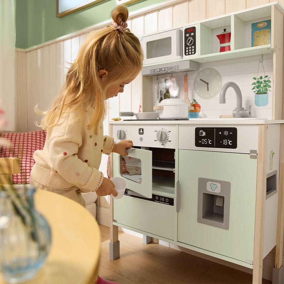 Enfant jouant avec une cuisine jouet en bois, comprenant un four, un micro-ondes et un réfrigérateur.