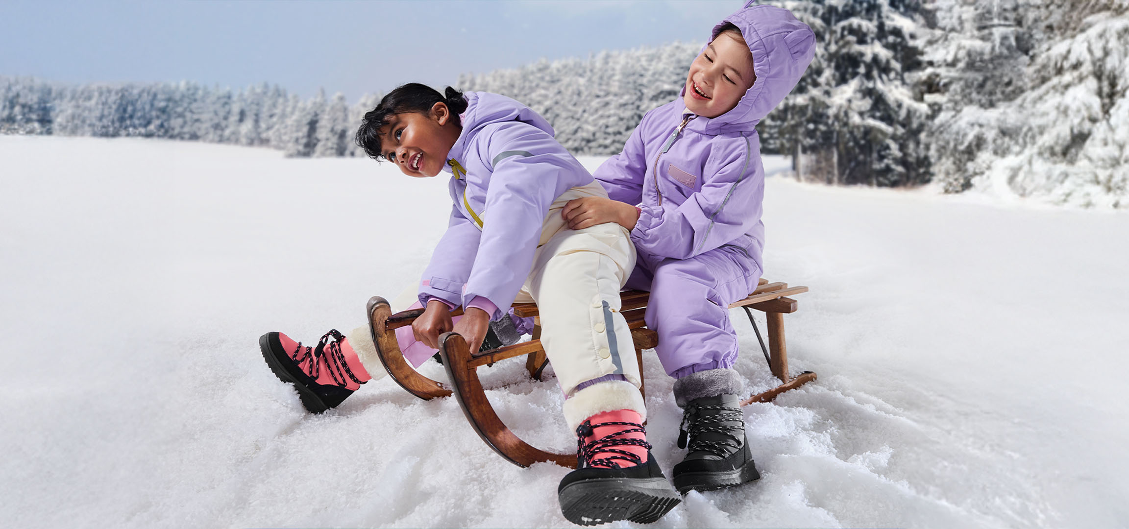 Deux enfants en combinaisons de neige violettes et bottes d'hiver font de la luge dans un paysage enneigé.