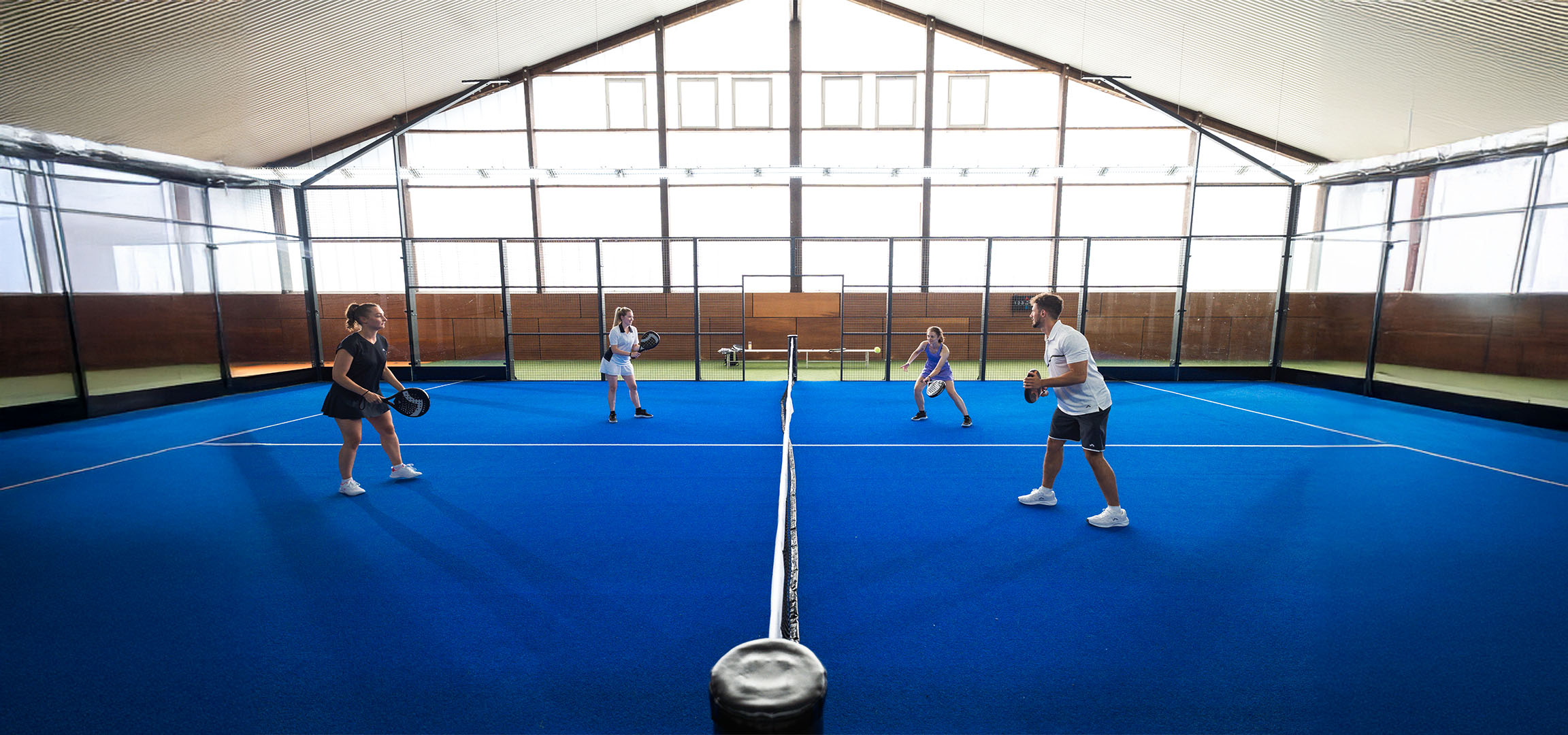 Quatre personnes jouent au padel sur un terrain bleu, avec raquettes et vêtements de sport.