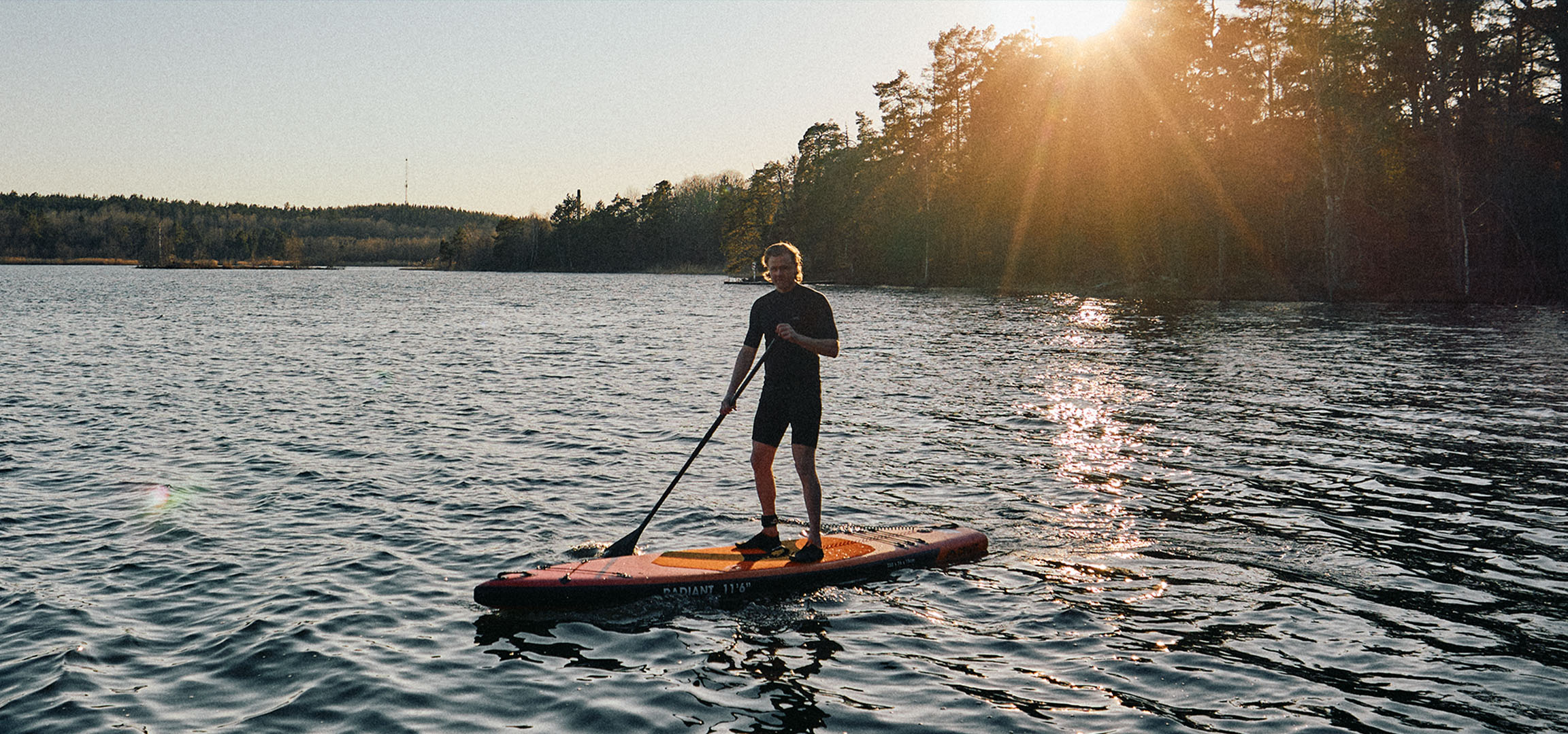 Homme sur une planche de stand up paddle sur un lac au coucher du soleil.