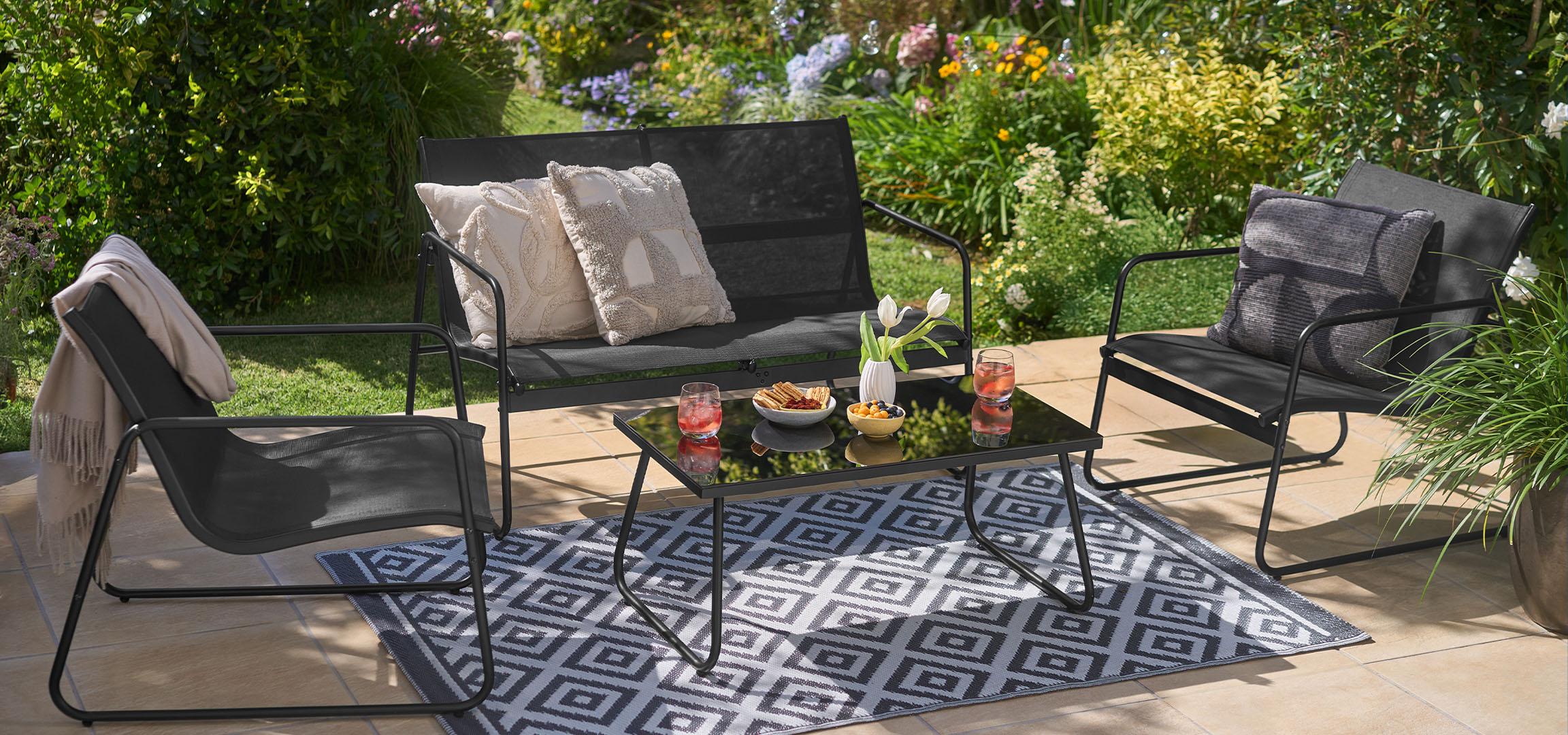 Ensemble de mobilier de jardin avec chaises noires, banc, table et tapis dans un jardin.