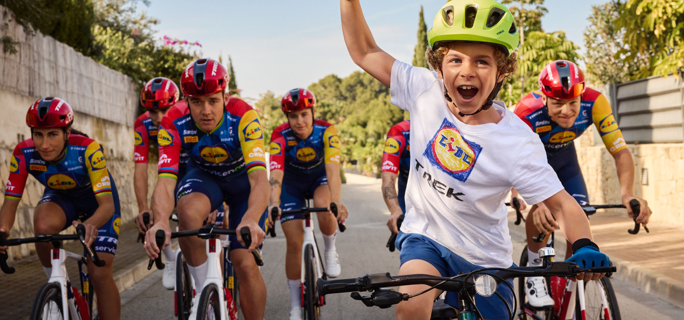 Enfant avec casque et t-shirt avec logo Lidl, entouré de cyclistes.