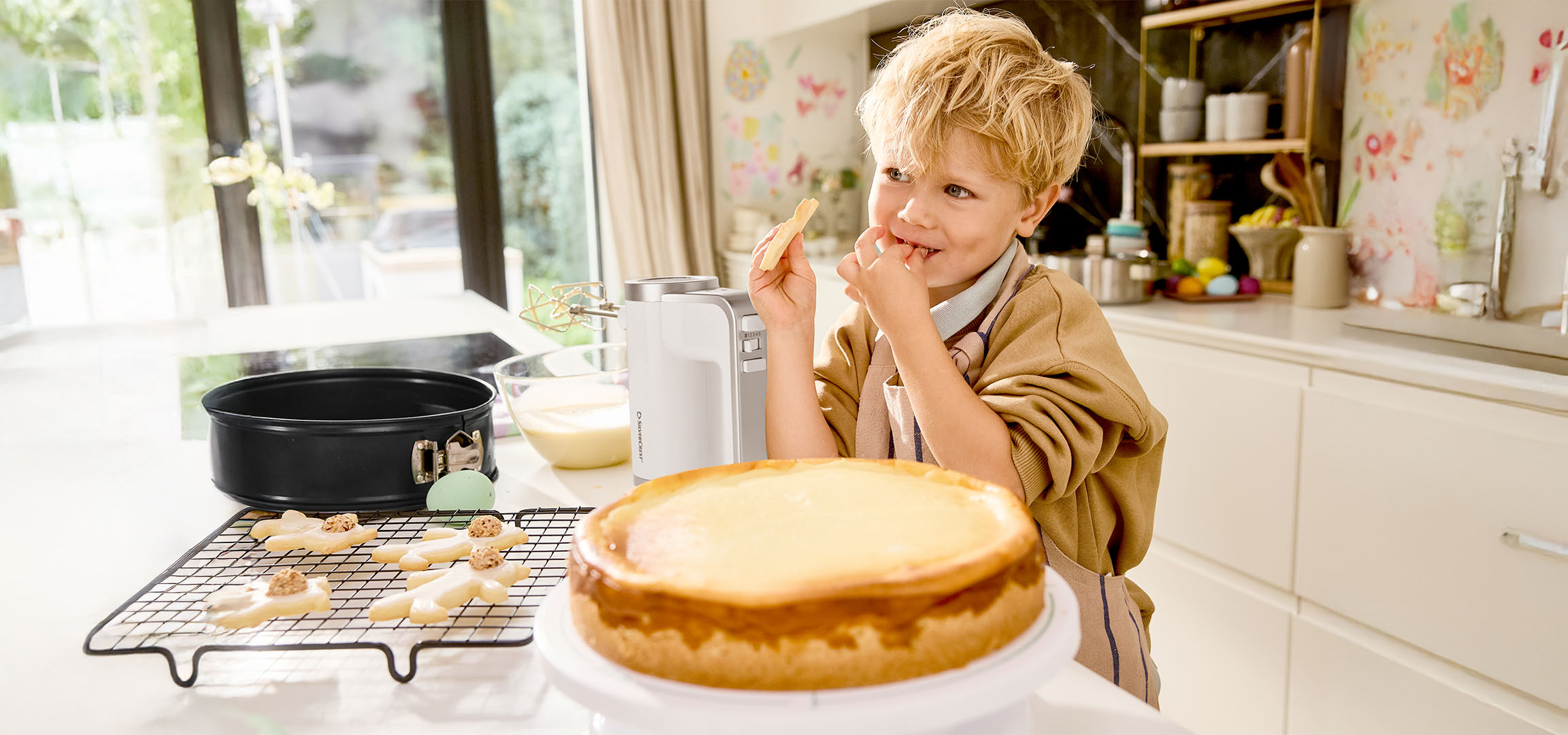 Un garçon goûte la pâte en préparant un gâteau et des biscuits dans la cuisine.