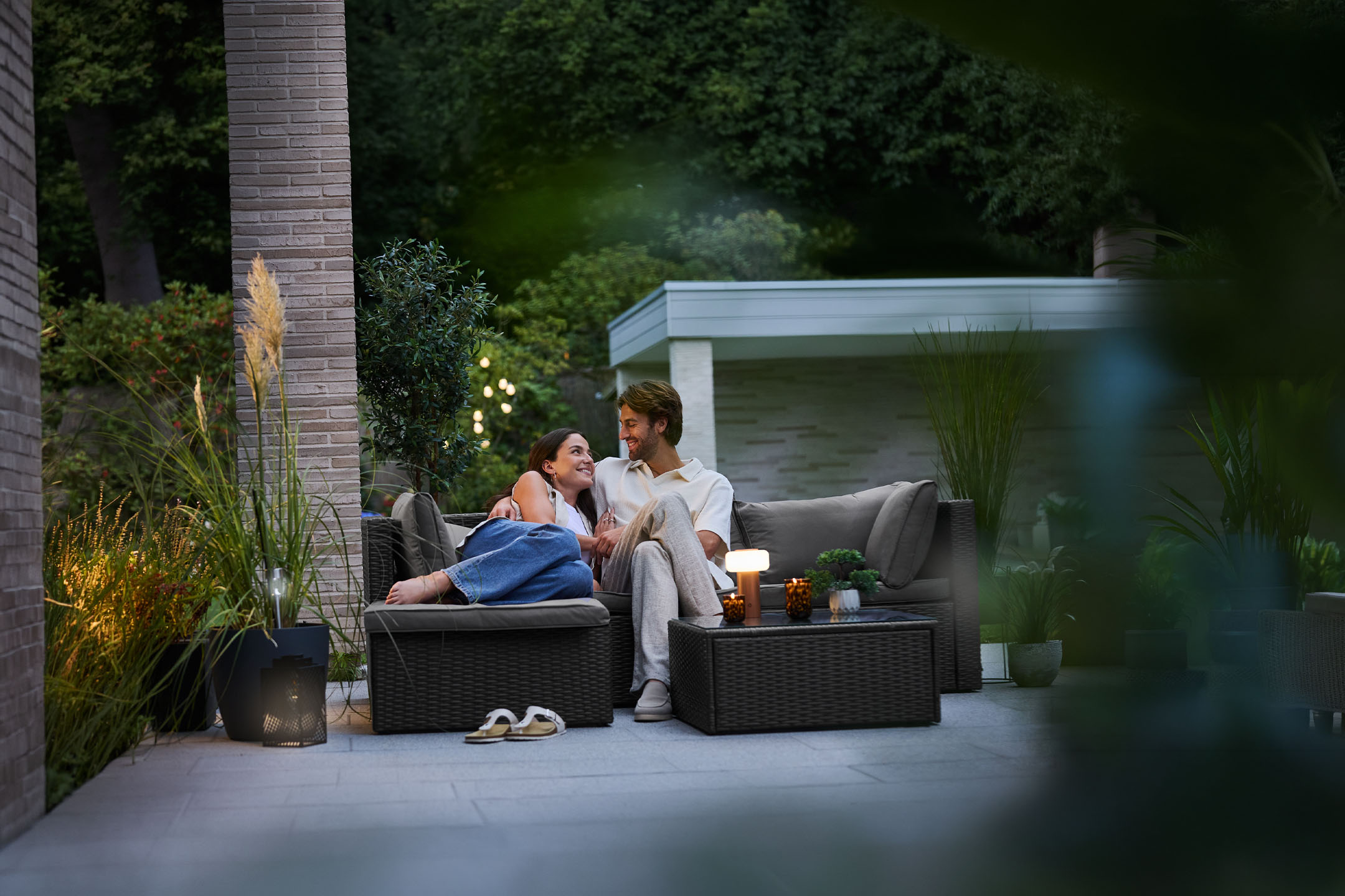 Couple se relaxant sur des meubles de jardin en rotin, éclairés par des lampes d'extérieur.