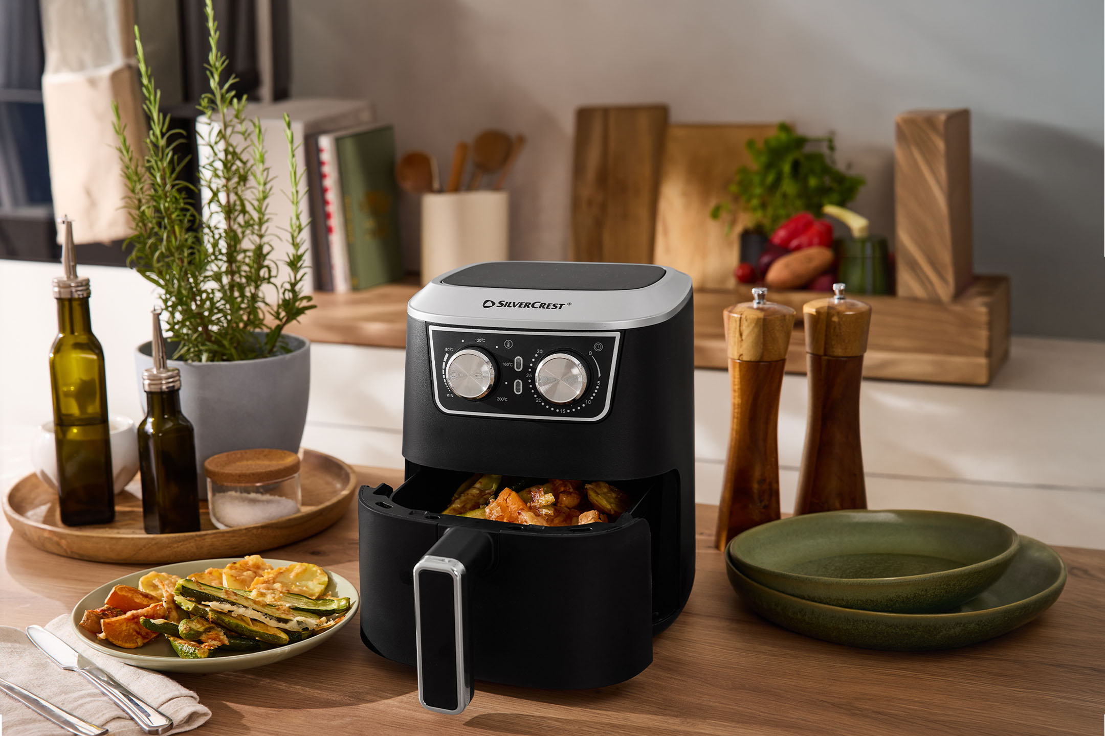 Friteuse à air avec légumes rôtis, huile d'olive, sel et poivre sur un comptoir de cuisine.