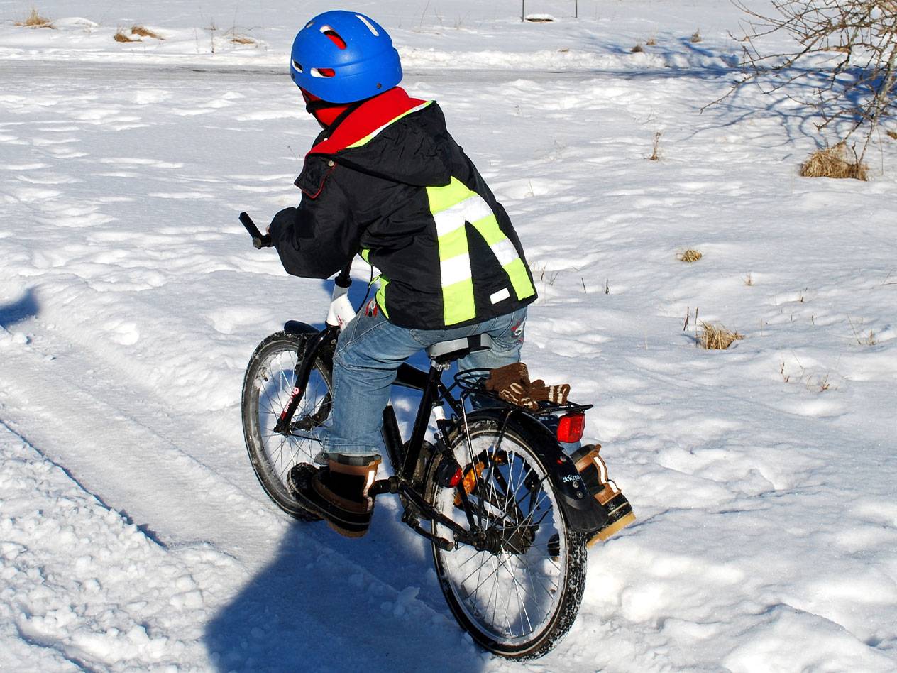Enfant avec un casque bleu et un gilet réfléchissant à vélo dans la neige.