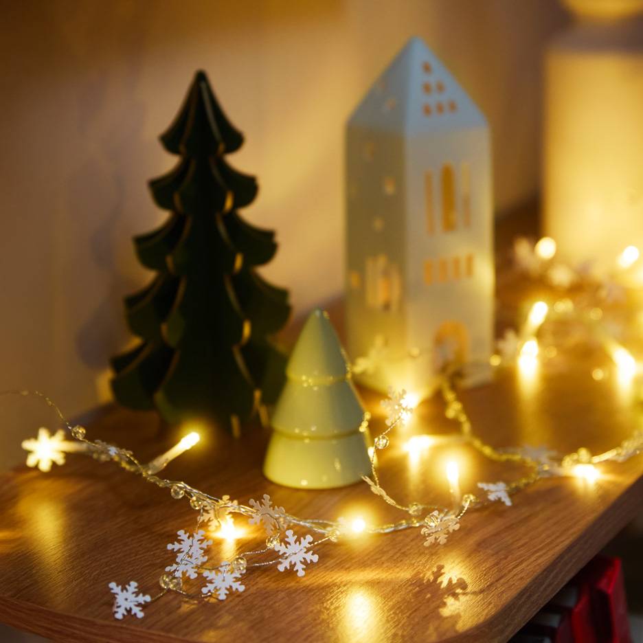 Décorations de Noël : un sapin vert foncé, un sapin vert clair, une maison blanche et une guirlande lumineuse avec des flocons de neige.