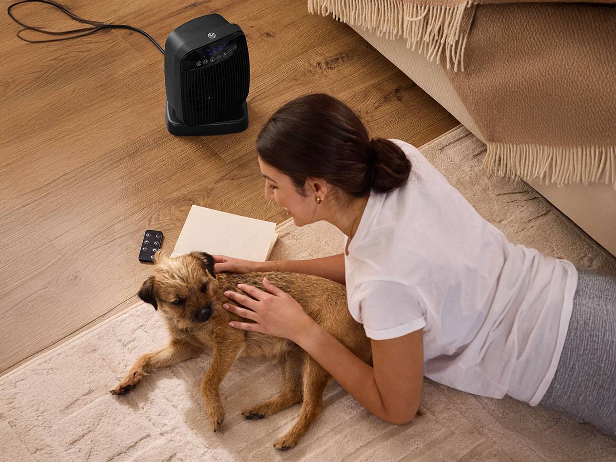 Femme caressant un chien à côté d'un radiateur noir au sol.